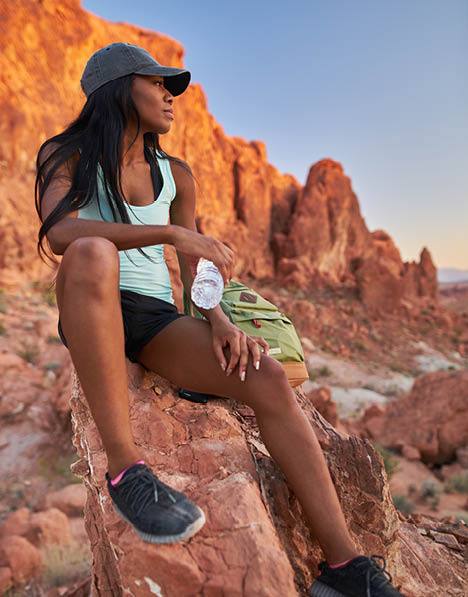 woman taking a break from hiking to drink water at valley of fire park in front of red rock formation